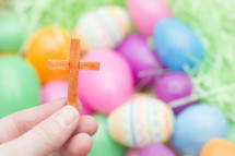 hand holding a small wooden cross and plastic Easter eggs