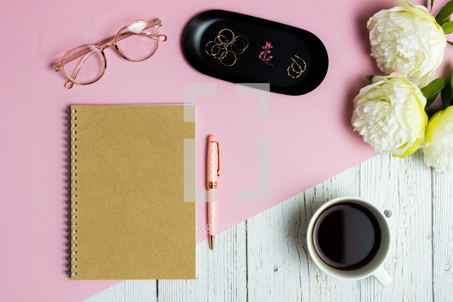 Notebook concept for women with pink, white roses and coffee over pink and wooden table.