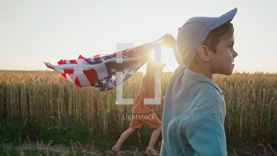 Cute little boys - American patriotic kids running with national flag on open area countryside road.
