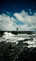 waves crashing into a rock wall near a lighthouse 