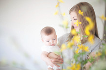 Mother holding infant daughter behind flowers.