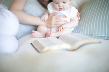 Mother holding daughter up on the bed as she looks at an open Bible.