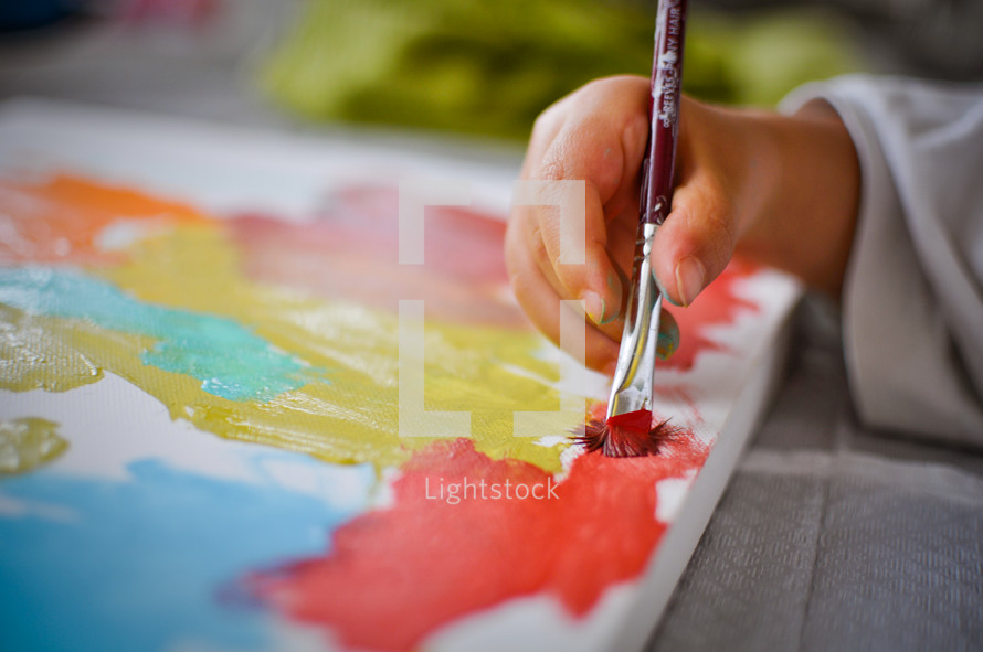 A child paints with colorful paints on a canvas.
