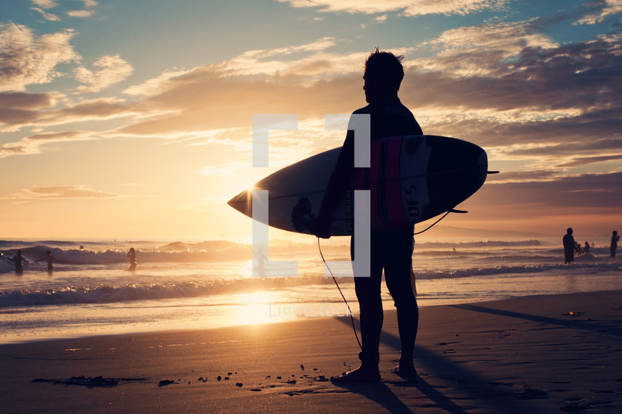 a man with a surfboard at sunset 