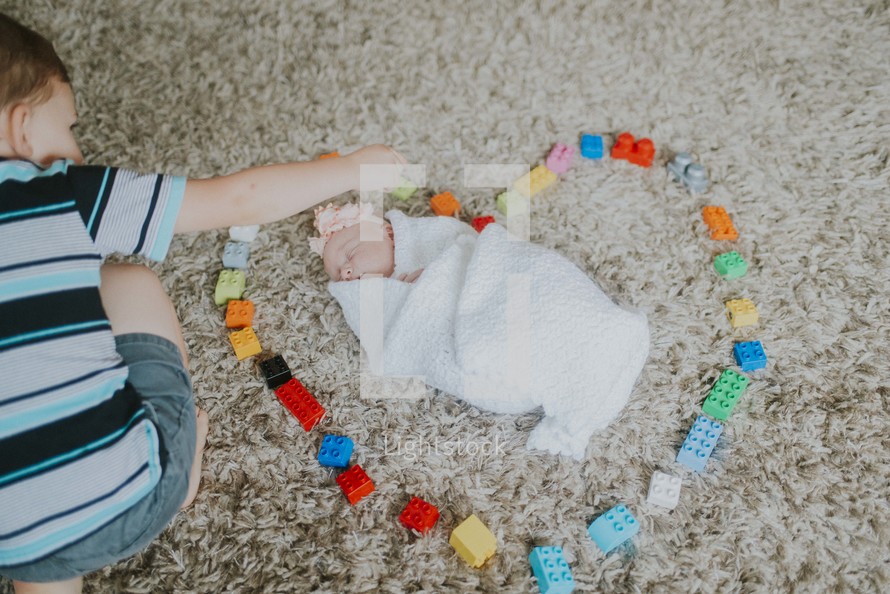 a big brother making a heart around his baby sister with legos 