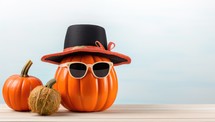 Halloween pumpkin with sunglasses and hat on wooden table with blue sky background