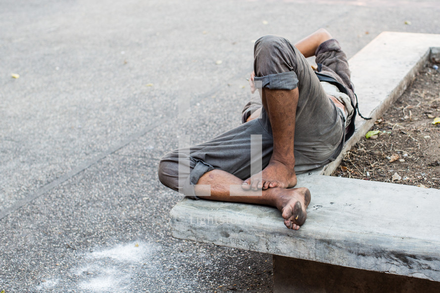 a homeless man sleeping on a concrete bench 