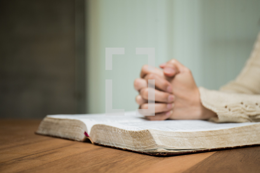 a woman with praying hands over an open Bible 