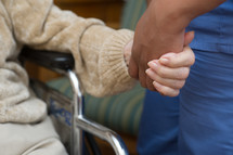 Hand of a caregiver holding hand of person on wheelchair.