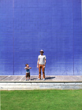 Father and son standing  a boardwalk in front of a brick wall.