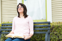A woman sitting on a bench with an open Bible in her lap, looking up.