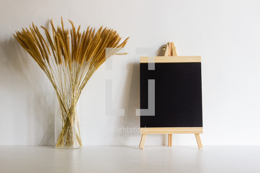 vase of brown fuzzy grasses and blank easel 