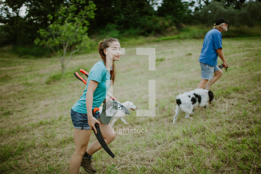 A man and woman walking their dogs through a mowed field.