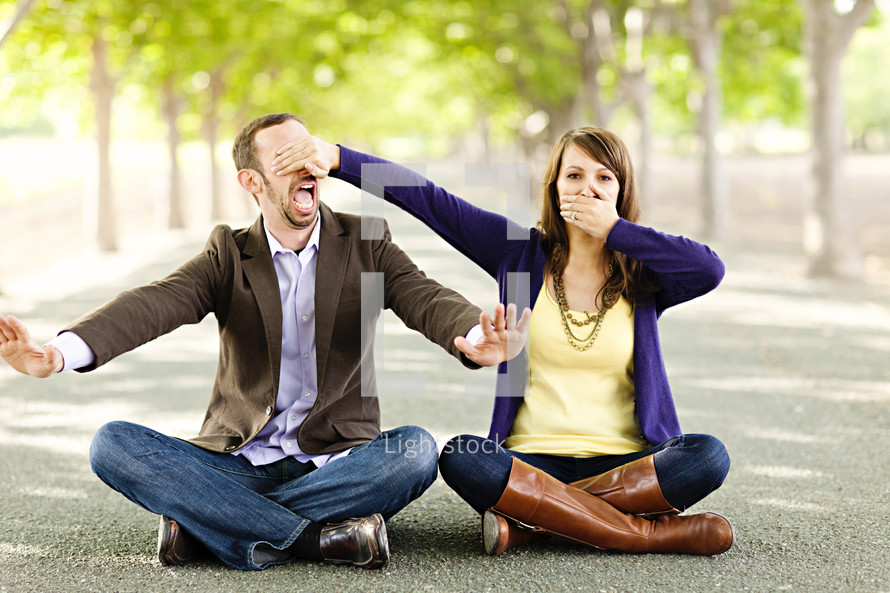 ear no evil speak no evil young engaged couple sitting indian style on ground 
