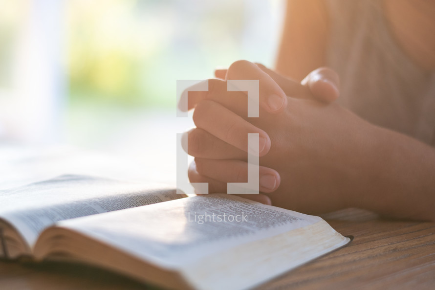 praying hands beside of a Bible 