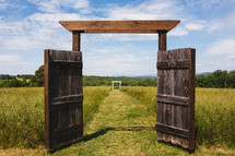 Open wooden gate doors leading to a pasture.