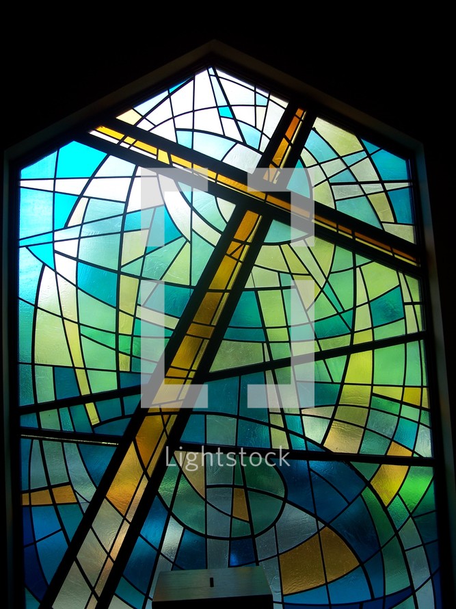 The power of the cross - Stained glass window art of the cross of Christ in shades of blue, green, gold and yellow showing the redeeming power of the Cross where Jesus was crucified and slain for the sins of mankind.