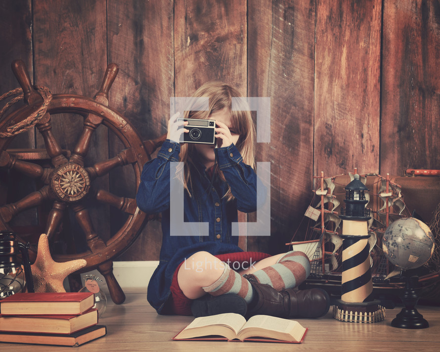 a little girl holding a camera and a nautical travel scene 