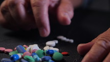 Grandmother counts multicolored tablets on black table at home. The concept of old age, medication, treatment. Close-up of hands with wrinkles.