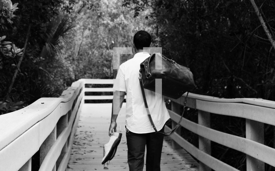 a man with a bag and shoes walking down a wooden path 