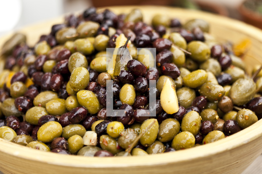 Bowl of black and green olives with garlic cloves and bay leaves.