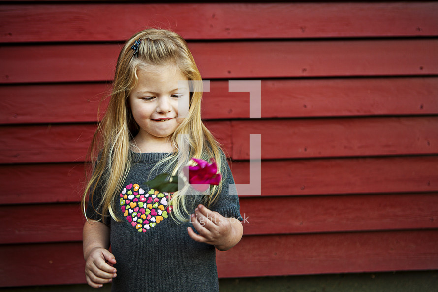 girl holding flower standing against wood plank wall