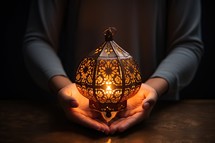 Female hands holding decorative lantern on dark background. Ramadan Kareem concept