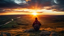 Hiker sitting on top of a mountain and looking at the sunset