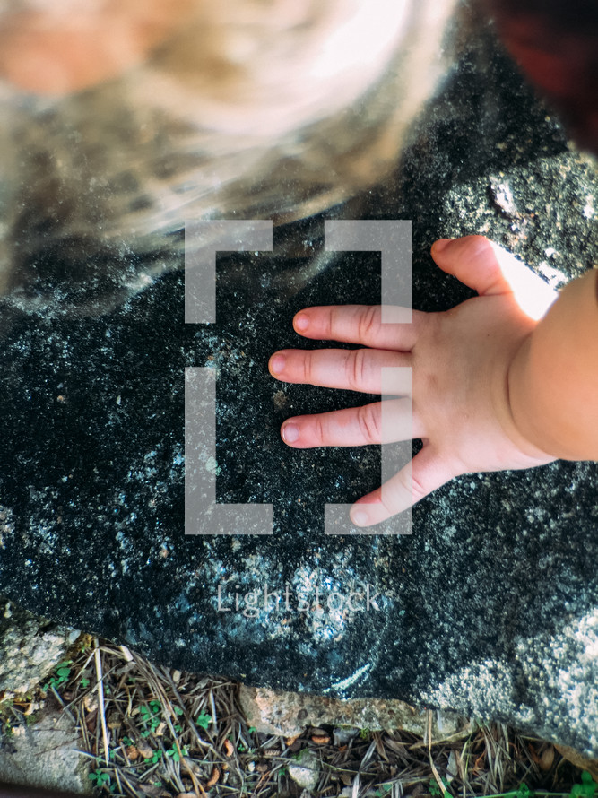 a toddler's hands on a rock 