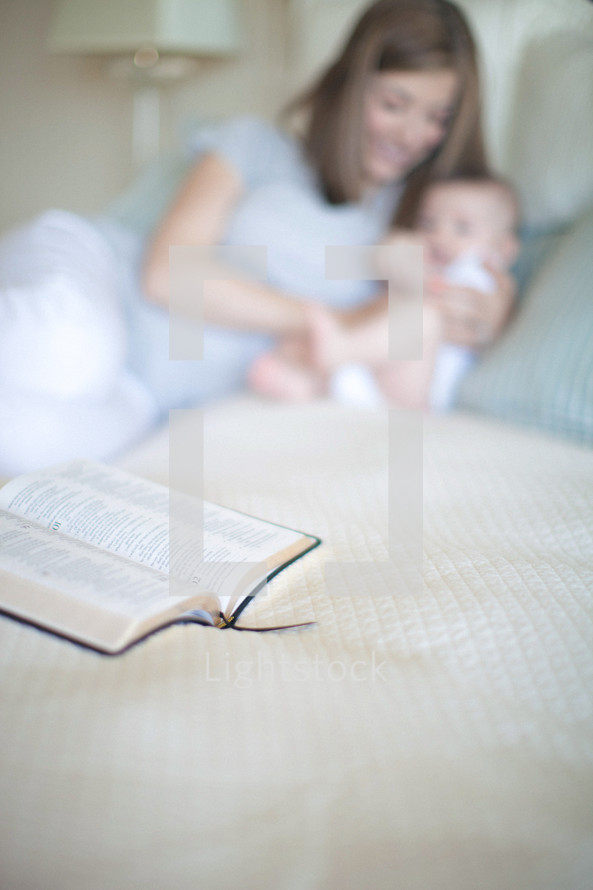 Mother holding infant daughter with open Bible on the bed.