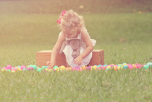 toddler girl with a stuffed bunny and Easter eggs in grass 