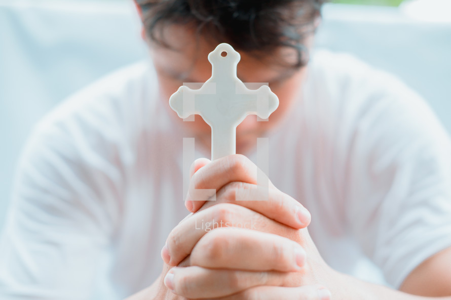 a man holding a cross praying with head bowed 