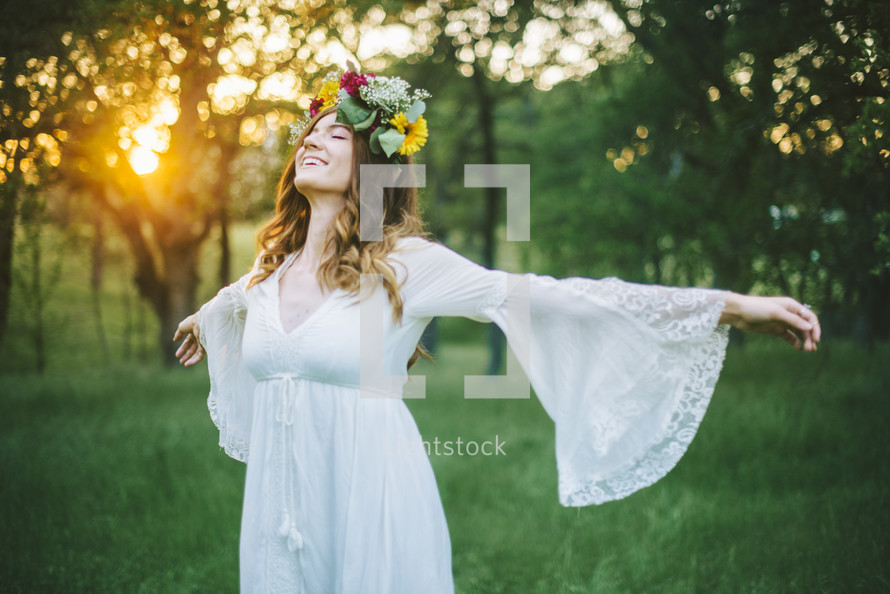 a woman standing in a field with outstretched arms with flowers in her hair 