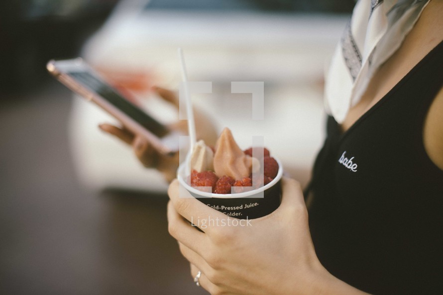 a woman with a cellphone and cup of frozen yogurt 