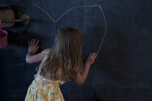 a toddler girl drawing a heart on a chalkboard 