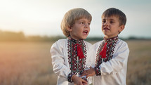 Beautiful portrait of little ukrainian boys singing song in wheat field after harvesting. Children in traditional embroidery vyshyvanka shirt. Ukraine, national costume, happy childhood future