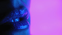 Fashion model, shiny gloss or lipstick on plump seductive lips. Neon studio light. Macro view of woman. Advertising make-up, beauty, cosmetics concept. High quality photo