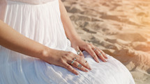 Woman in white dress and boho rings on hands sits on sandy beach alone. Meditation, immersion in inner world, unity with nature. High quality photo