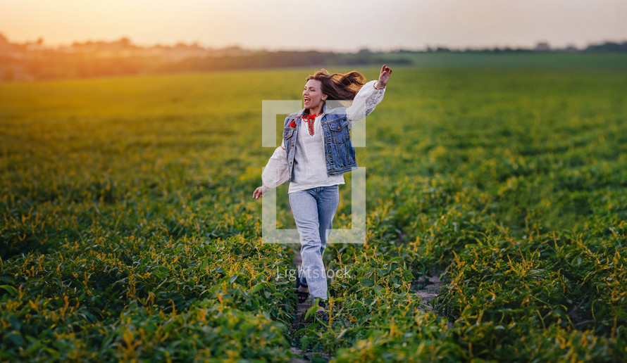 Happy stylish woman running in green field. Young lady in white embroidery shirt. Freedom, summer, love, ethno, folk lifestyle. 