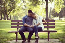 Man comforting his wife on a park bench. 