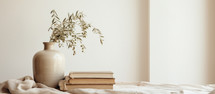 Home interior. Vase with dried olive branches and books on white table