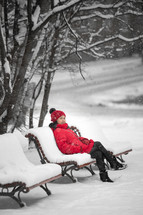 a woman in a red coat sitting on a bench in snow 