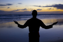 silhouette of a man in worship on a beach 