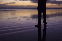man's legs standing on wet sand on a beach 