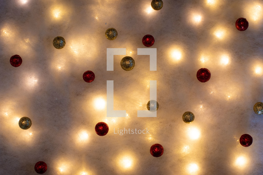 Red and gold ornaments on fake snow backdrop with lights