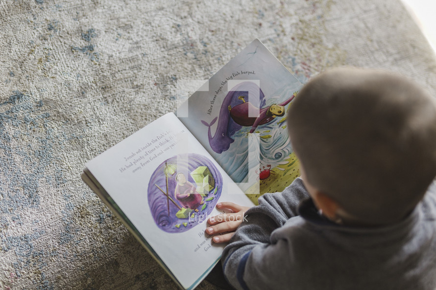 Little boy reading a picture book of the Bible story of Jonah.