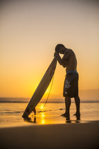 surfer with his head bowed in prayer over his surfboard