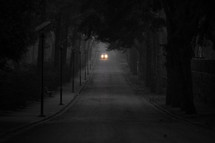 vehicle with headlights driving down a dark road 