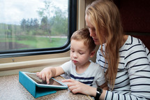 Son and his mom with tablet PC in the train