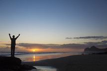 silhouette of a man standing with raised hands on a beach 